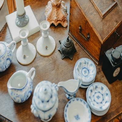 Xícara de porcelana azul e branca compondo um conjunto de peças clássicas sobre mesa de madeira com objetos decorativos em estilo tradicional.