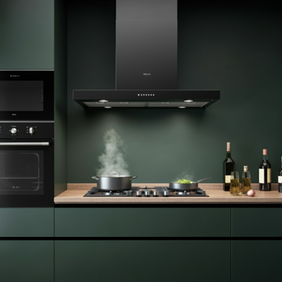 Coifa de parede preta instalada sobre cooktop, realizando a sucção de fumaça durante o preparo de alimentos.