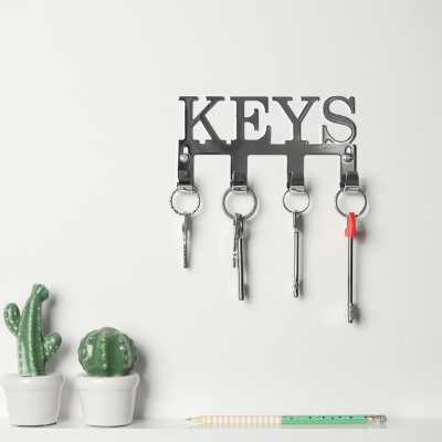 Porta-chaves de parede preto com a palavra “KEYS” e quatro ganchos com chaves, instalado sobre parede branca.