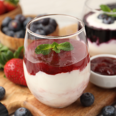 Geleia de frutas vermelhas com creme em taça de vidro, acompanhada de morangos e mirtilos.