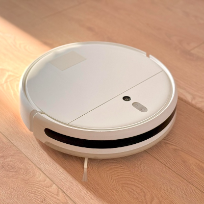 Aspirador de pó robô branco realizando a limpeza automática de piso de madeira.