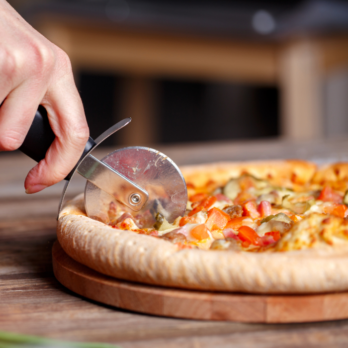 Pessoa cortando uma pizza com um cortador de pizza de lâmina circular sobre uma tábua de madeira.