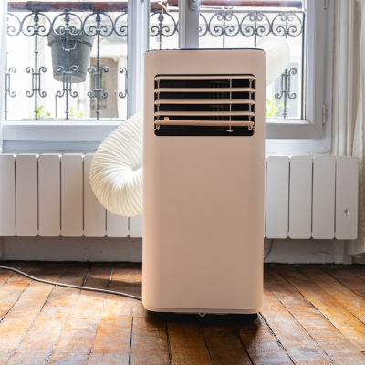 Ar-condicionado portátil branco com duto de exaustão instalado próximo à janela.